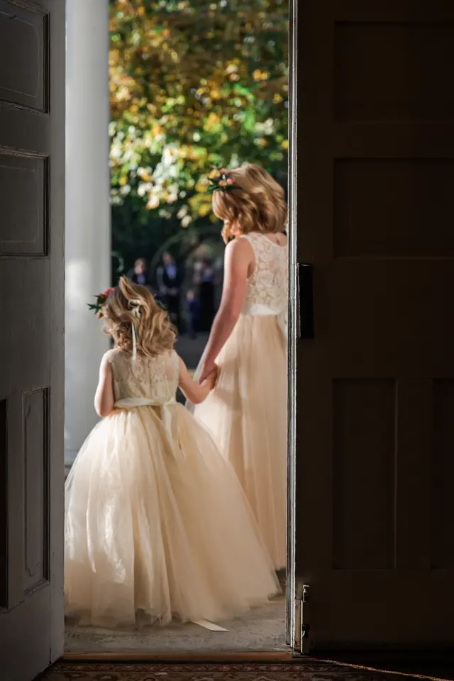 Flower girl and bride looking out through a dark doorway