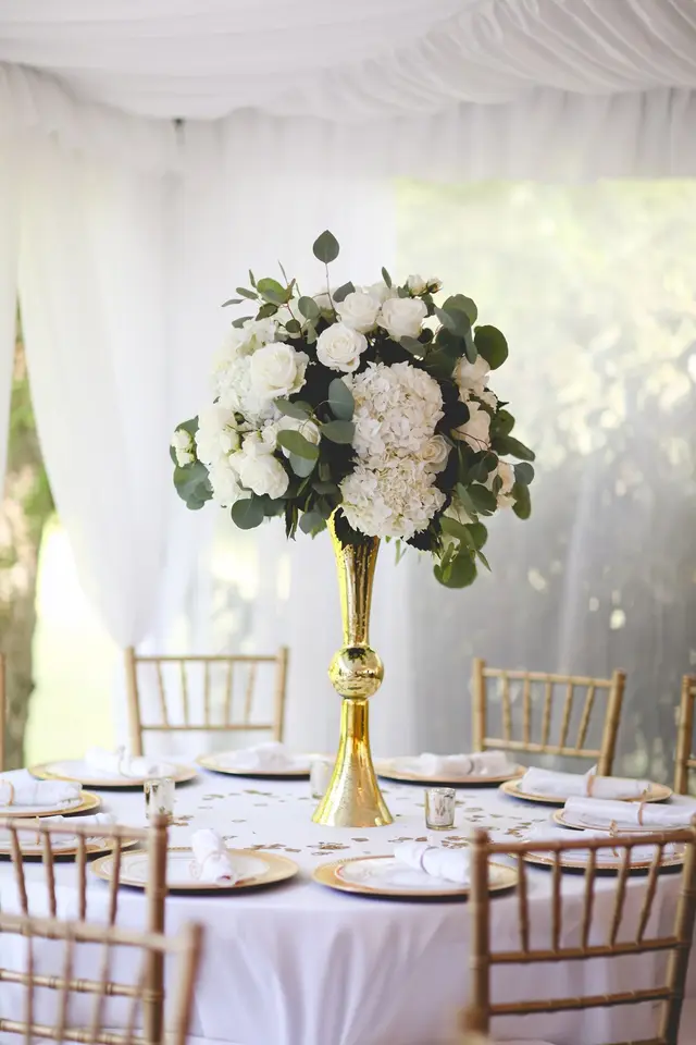 Tall centerpiece of white flowers on a table under a white tent