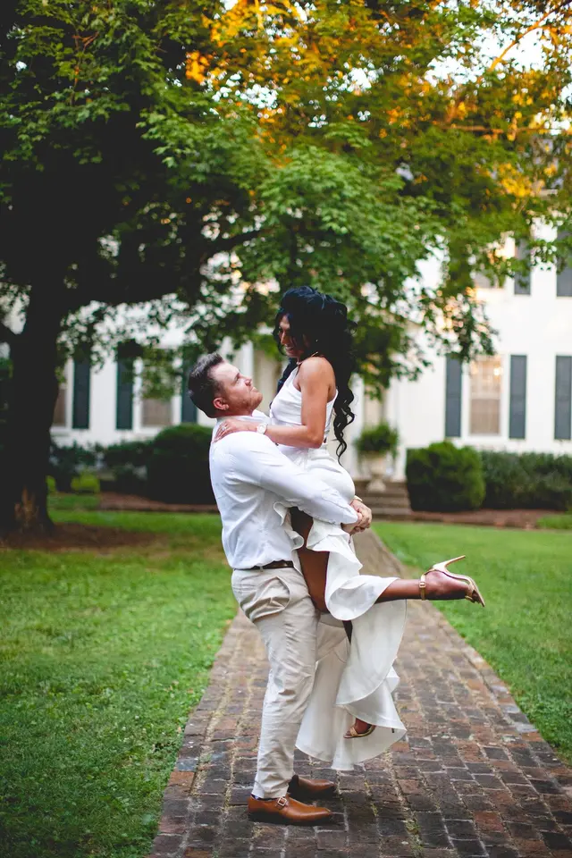 Groom lifting the bride on the brick walk in front of the house