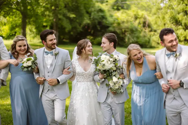 Wedding party in light blue and gray walking arm in arm across the lawn