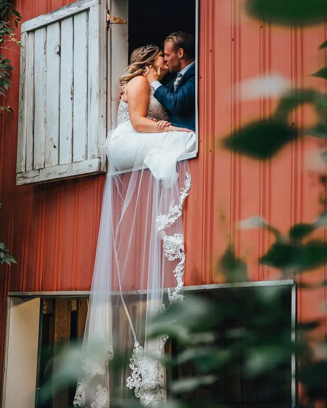 Couple kissing in the open hayloft door of the red barn