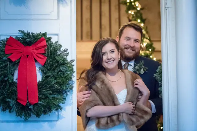 Winter couple, the bride in a fur stole beside a red-bowed wreath