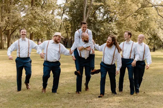 Groomsmen in suspenders horsing around on the lawn