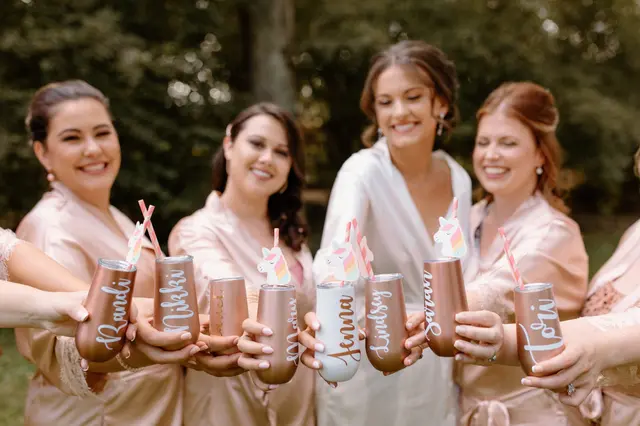 Bridesmaids in pink robes holding up personalized tumblers