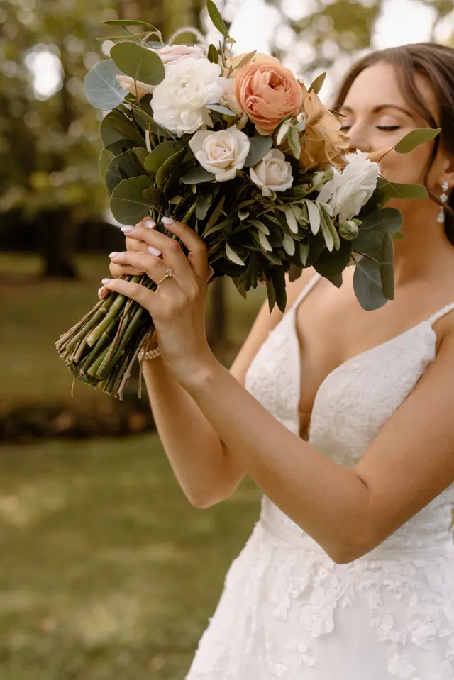 Bride breathing in her bouquet of white and peach roses