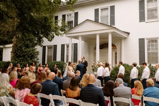 Guests seated for a ceremony on the front lawn beside the portico