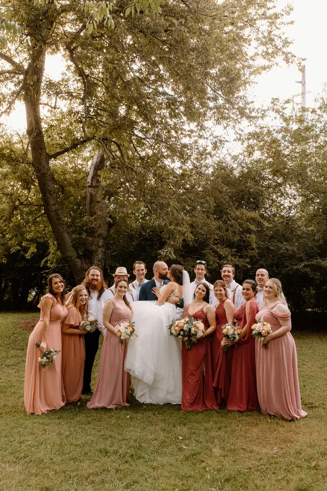Bridesmaids in pink and red around the couple under the trees