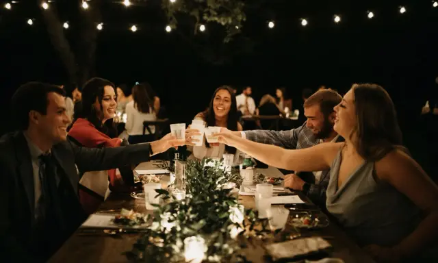 Guests toasting across a long table under string lights at night