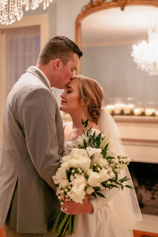 Groom kissing the bride's forehead in the parlor