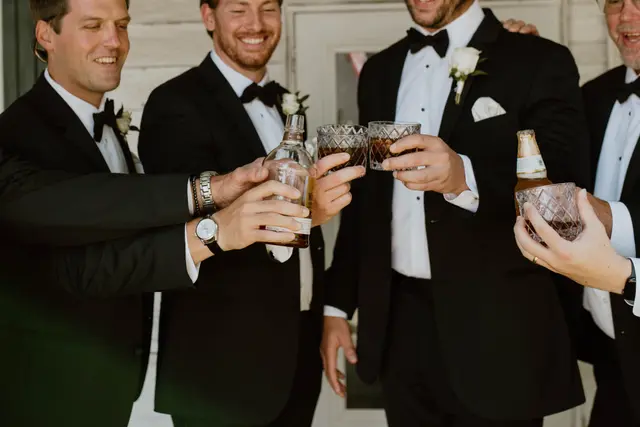 Groomsmen in tuxedos raising their glasses