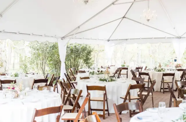 Round tables and wooden chairs under an open-sided white tent