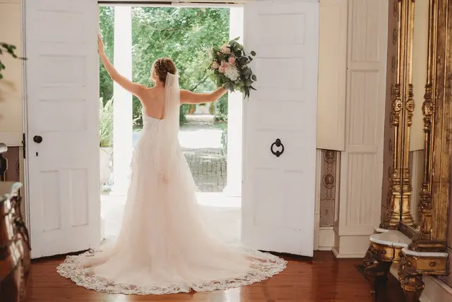 Bride in the open front doors with her bouquet raised
