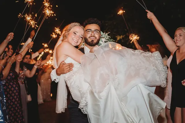 Groom carrying the bride through a sparkler send-off at night
