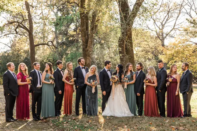 Large wedding party in jewel tones lined up under the trees