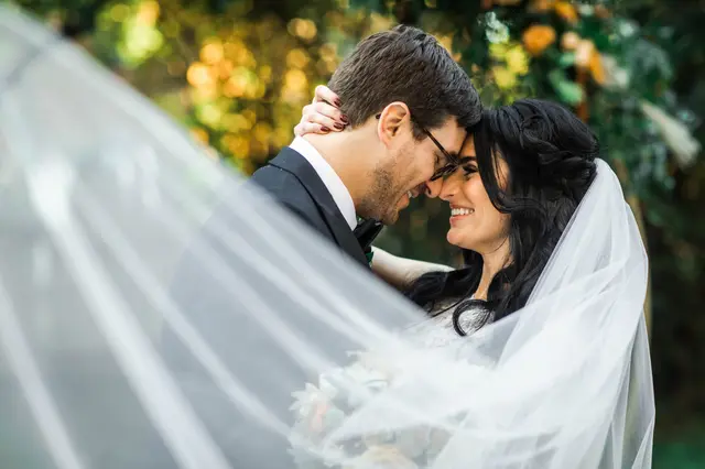 Couple wrapped in the bride's veil, foreheads touching