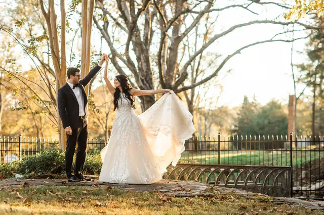 Groom twirling the bride beside the iron fence at sunset