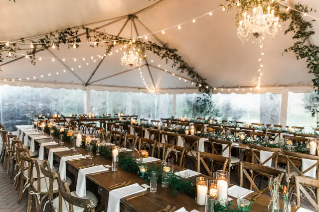 Long farm tables with candles under a tent strung with lights and chandeliers