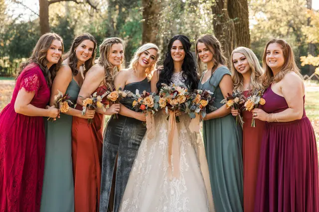 Bride with her bridesmaids in red, rust and sage gowns