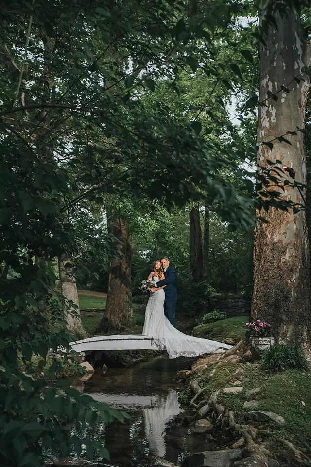 Couple on the footbridge in the shaded woods, reflected in the stream