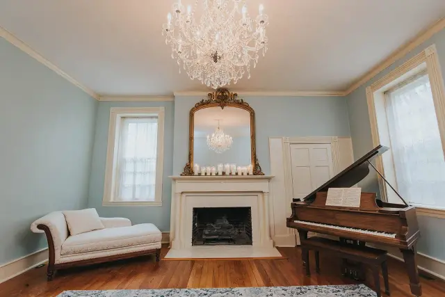Blue parlor with a crystal chandelier, fireplace, chaise and grand piano