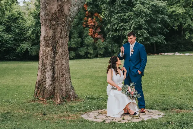 Bride seated on a stone circle under a big tree, the groom beside her