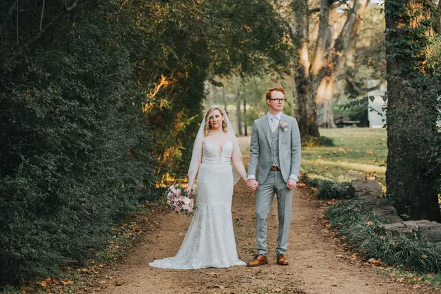 Couple holding hands on the gravel lane between tall hedges