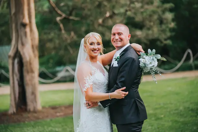 Bride and groom smiling beside a hollow tree on the lawn