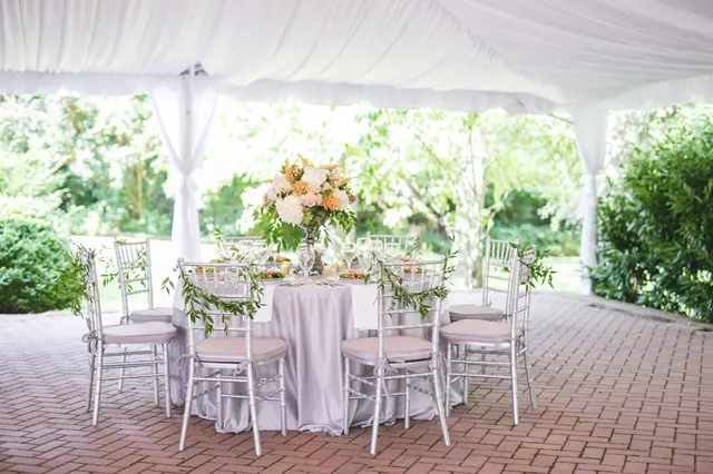 Table with silver chairs and peach flowers under a tent on a brick patio